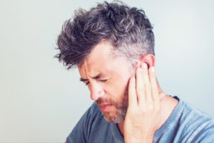 Middle-aged man holding his ear wincing in pain.
