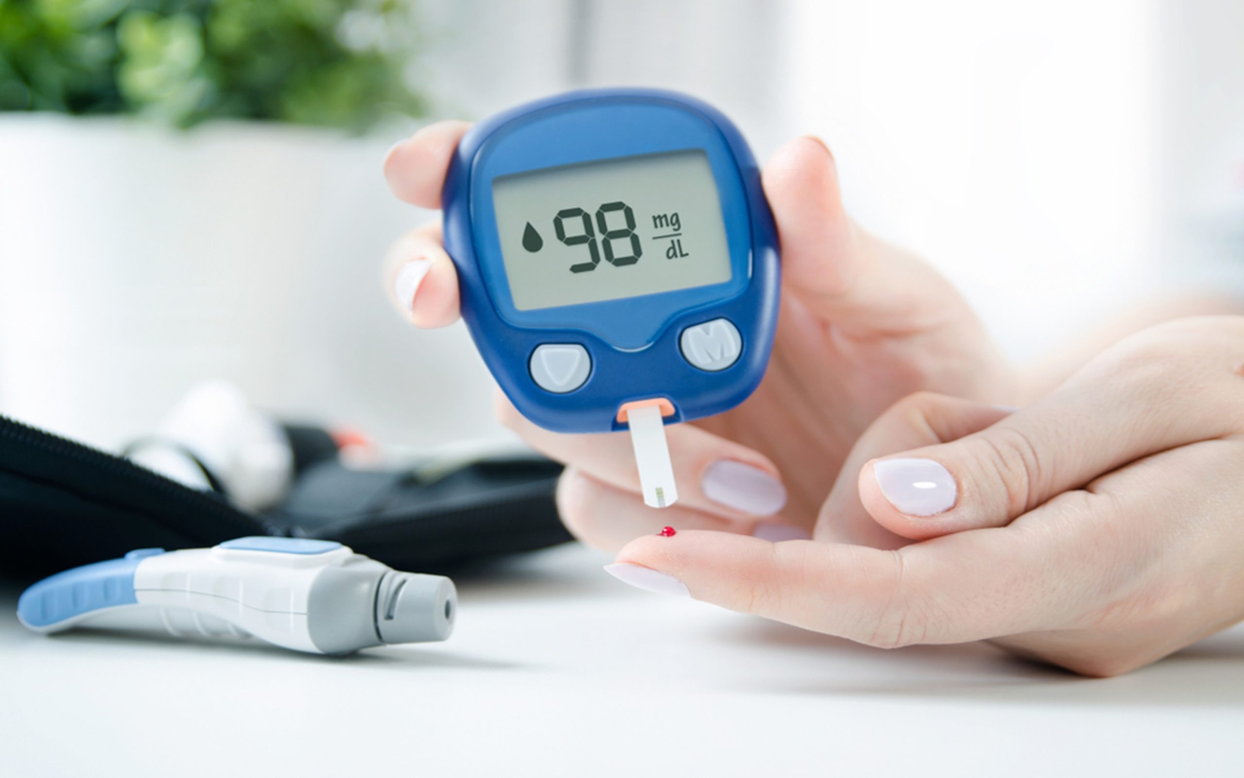 A close-up image of a woman checking her glucose levels with a blood sugar monitor.