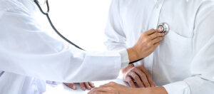 A closeup image of a doctor in a white coat holding a stethoscope to a patient’s chest.
