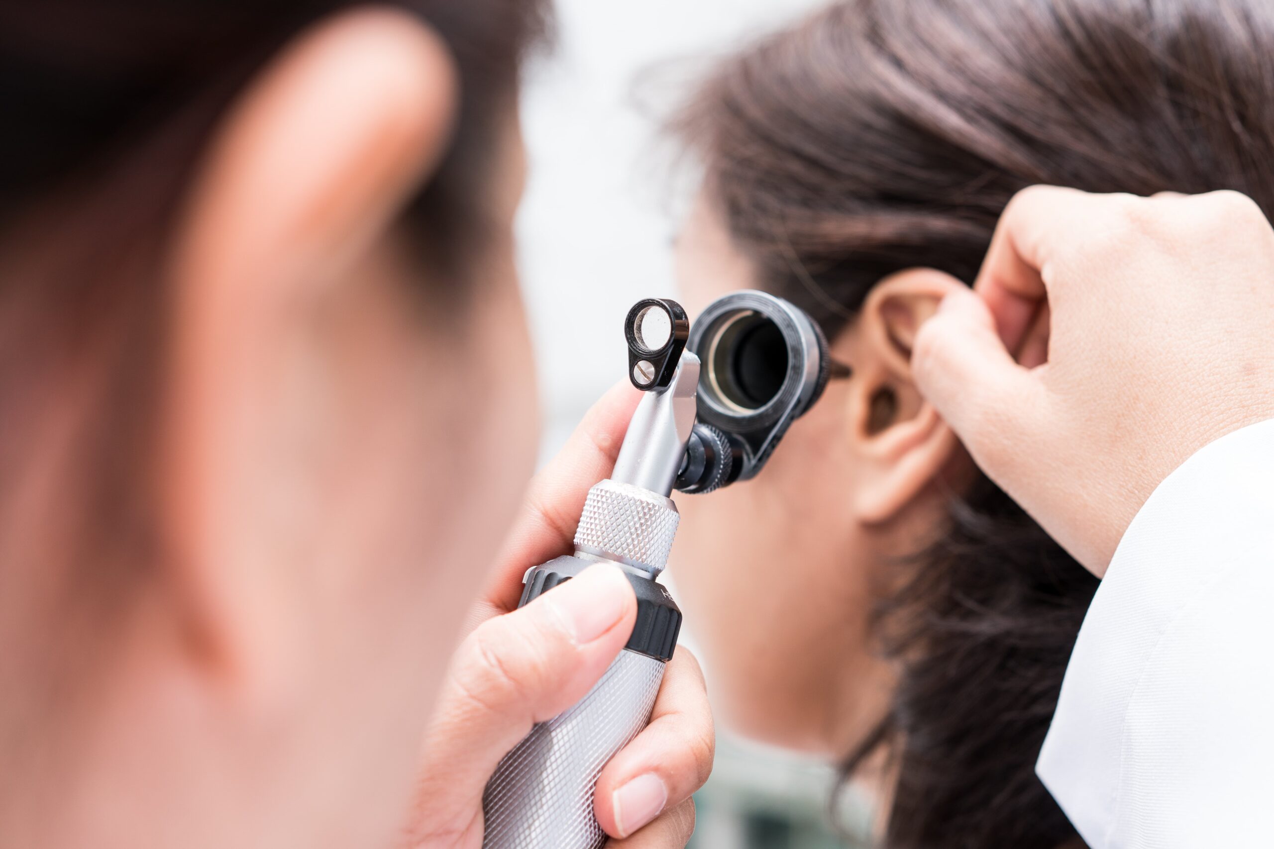 A closeup image of a doctor examining a woman’s ear canal using an otoscope.