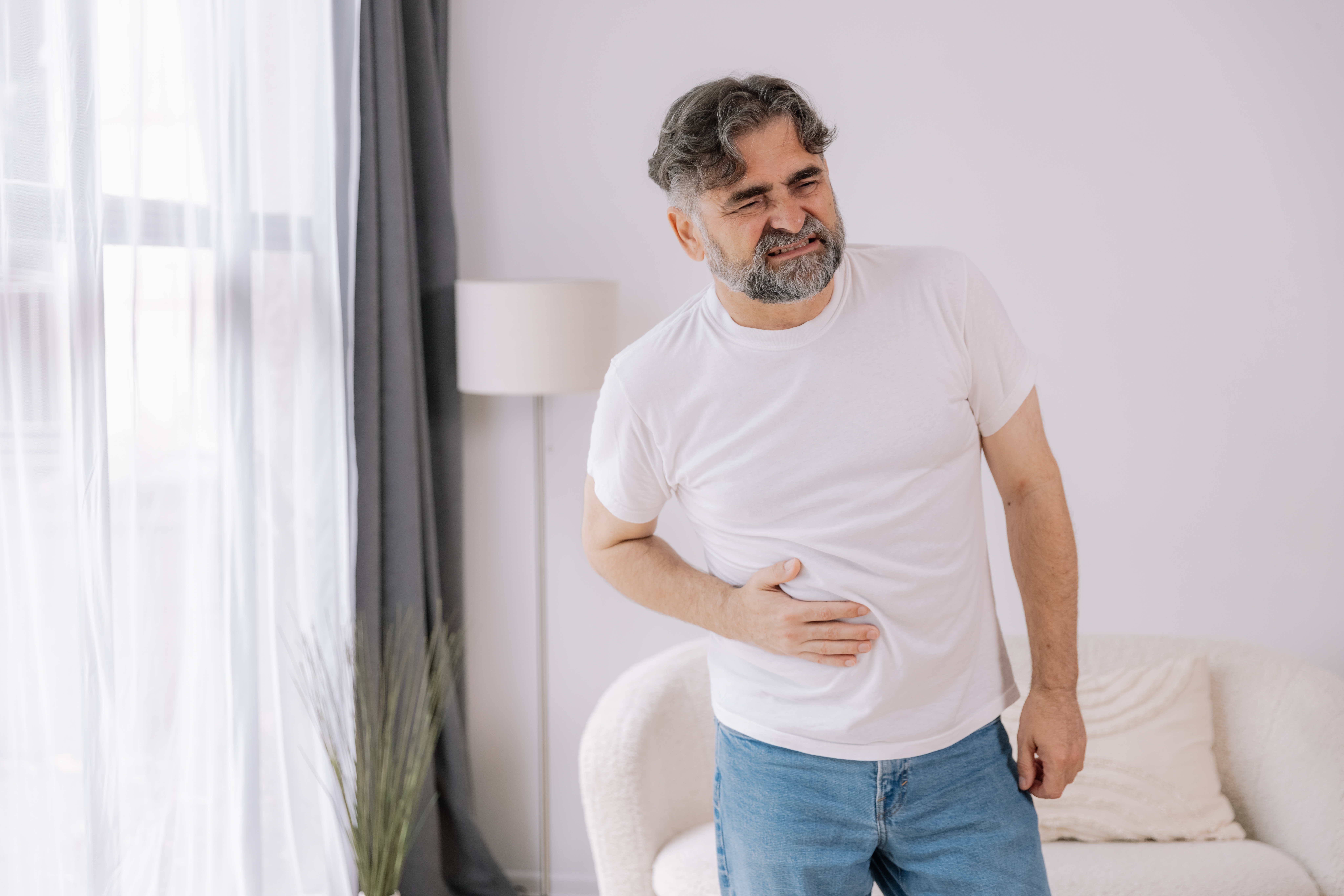 Older man suffering from right abdominal pain and holding his side at home
