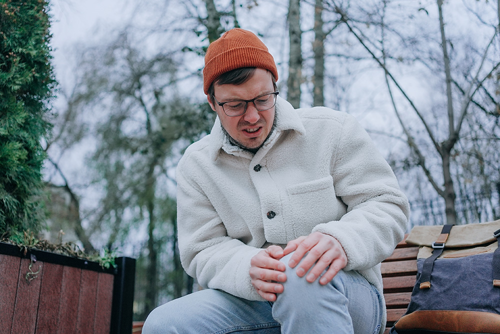 A man dressed for cold weather clutches his knee joint in pain