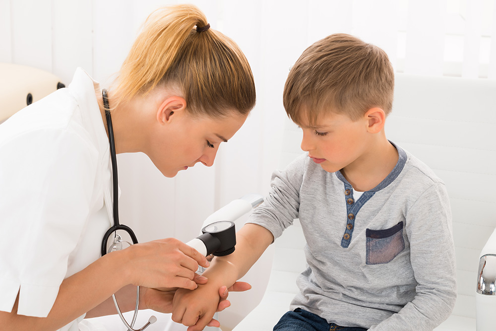 Doctor inspecting the skin of a young boy’s arm.